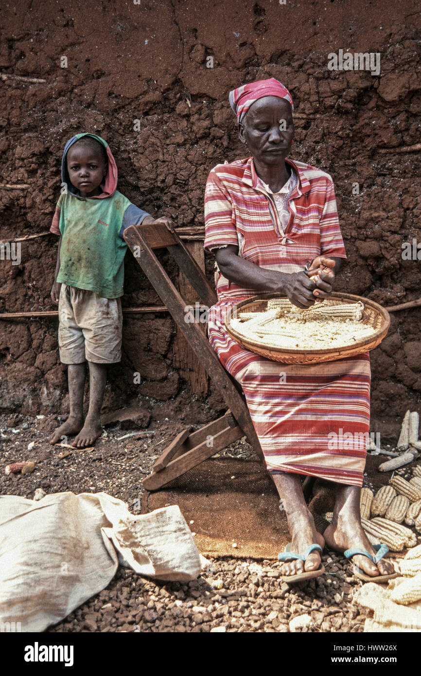 Eine alte Frau entfernt Kerne von einem Maiskolben ihr Enkelkind beobachtet sie, Himo, Kilimanjaro Region, Tansania Stockfoto