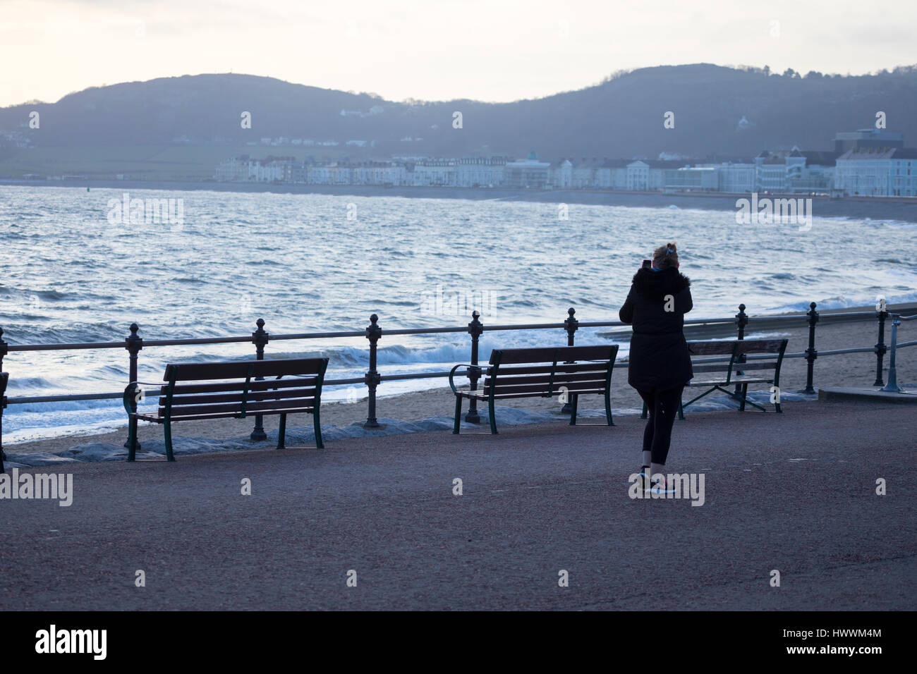 Eine Frau, die ein Bild mit ihrem Telefon während eines frühen Morgens Fuß entlang der beliebten Strandpromenade am Resort Stadt von Llandudno in der Cowny Grafschaft, Nord-Wales bei Sonnenaufgang Stockfoto