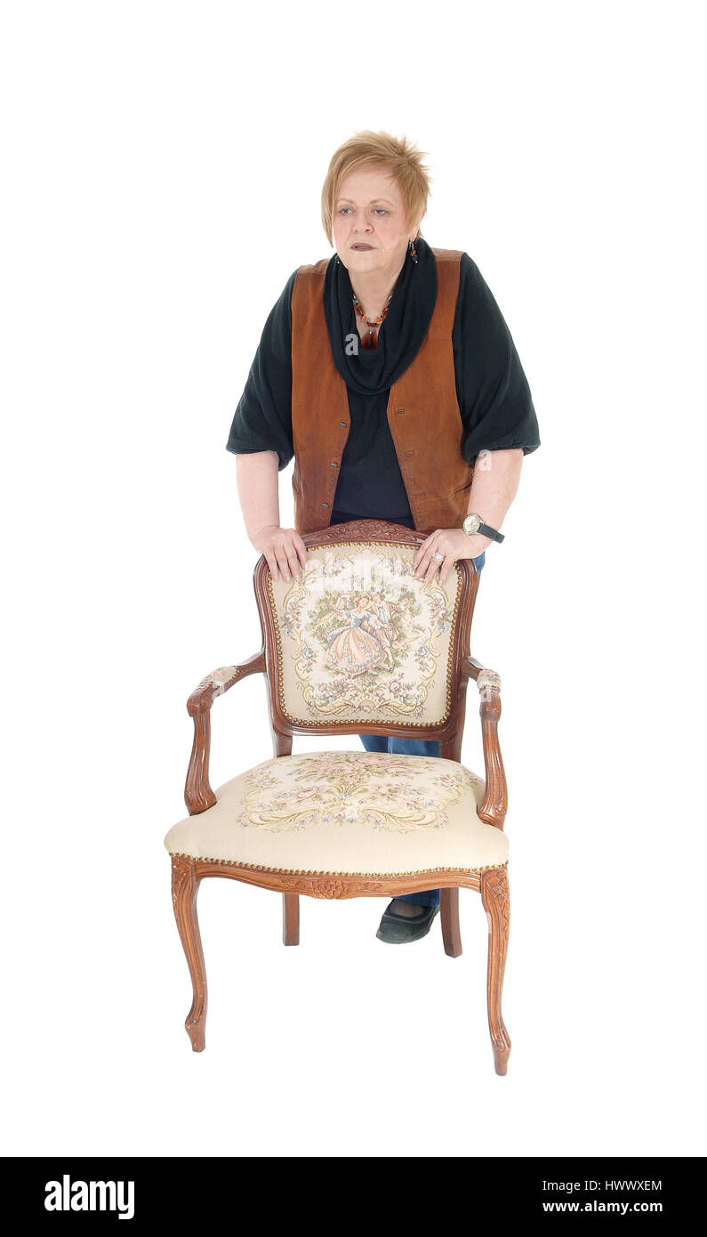 Eine ältere Frau in den Siebzigern stehen hinter einem alten Sessel, ernst, für weißen Hintergrund isoliert. Stockfoto