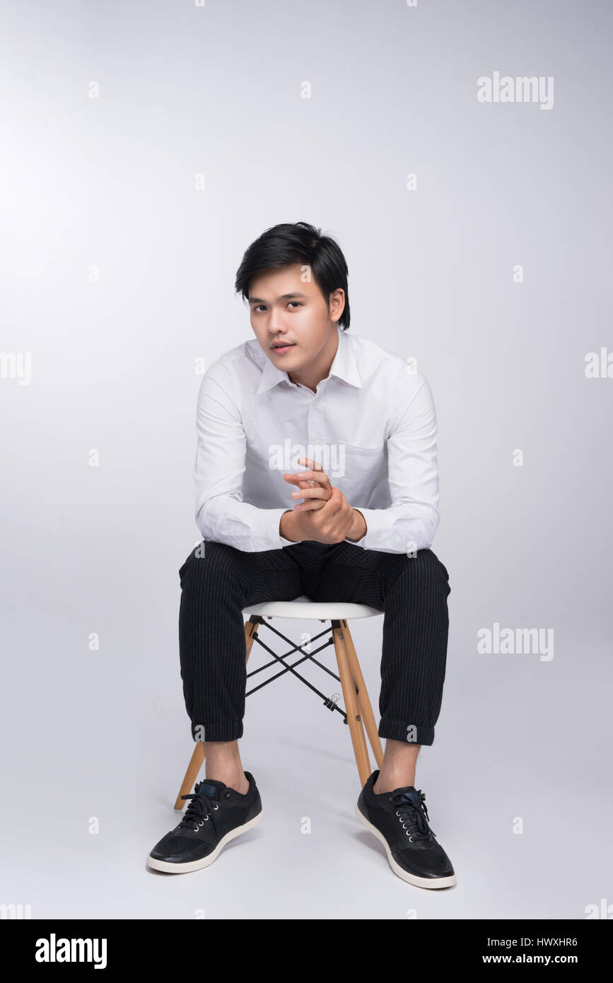 Smart casual asiatischen Mann sitzend auf Stuhl, posiert beim wegsehen in Studio-Hintergrund Stockfoto