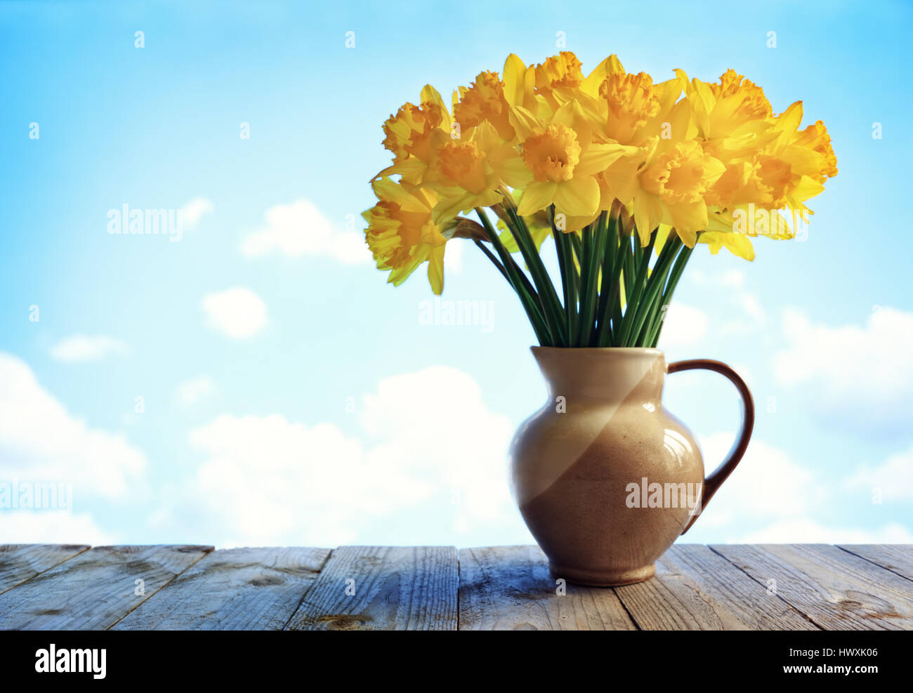 Vase voller Narzissen Blumen auf Holztisch vor einem blauen Himmel Stockfoto