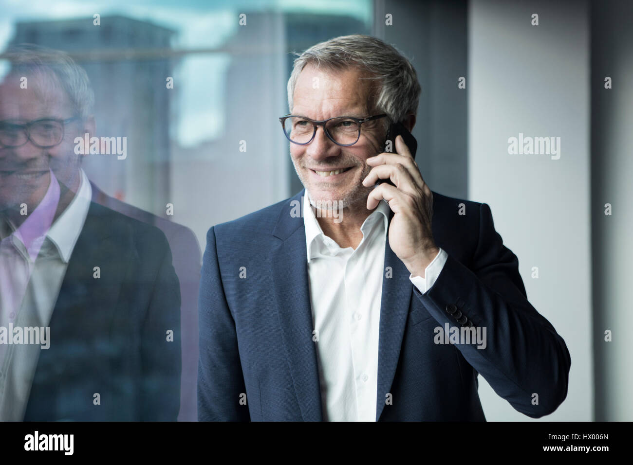 Lächelnde Geschäftsmann auf Handy am Fenster Stockfoto