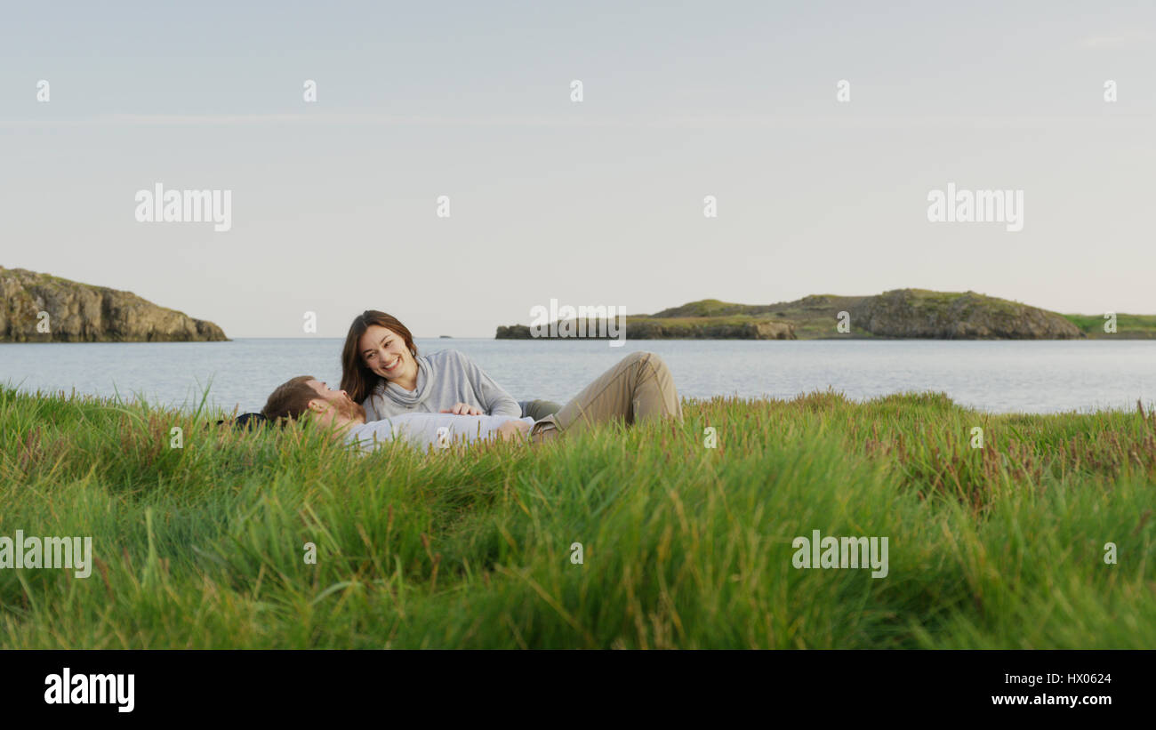 Lächelnd, Freund und Freundin Verlegung auf Wiese in der Nähe von See in abgelegenen Landschaft unter blauem Himmel Stockfoto