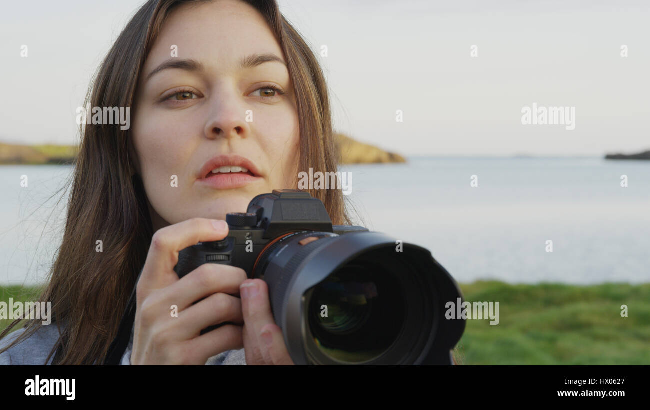 Nahaufnahme des Fotografen halten Kamera in Feld am See in abgelegenen Landschaft unter blauem Himmel Stockfoto