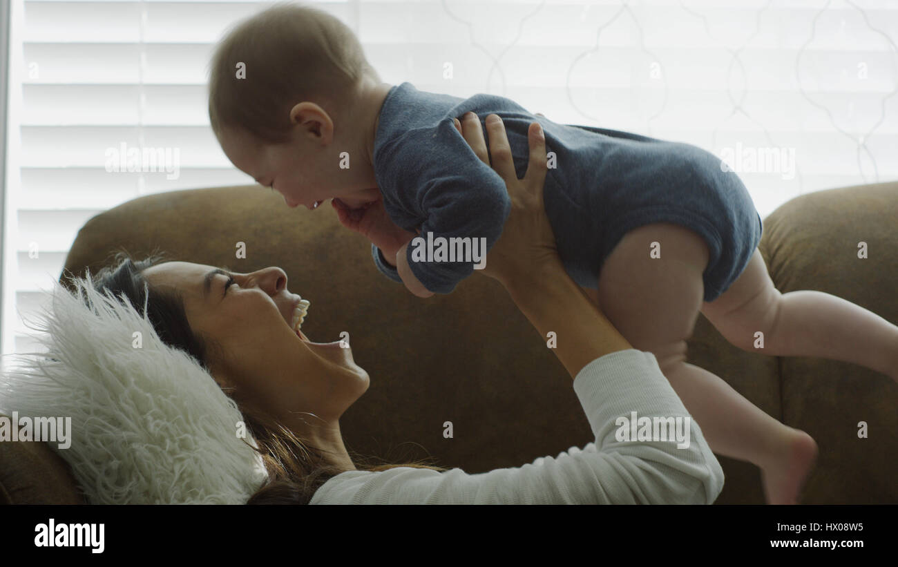 Profil von lachenden spielerische Mutter Baby Sohn halten und spielen auf sofa Stockfoto