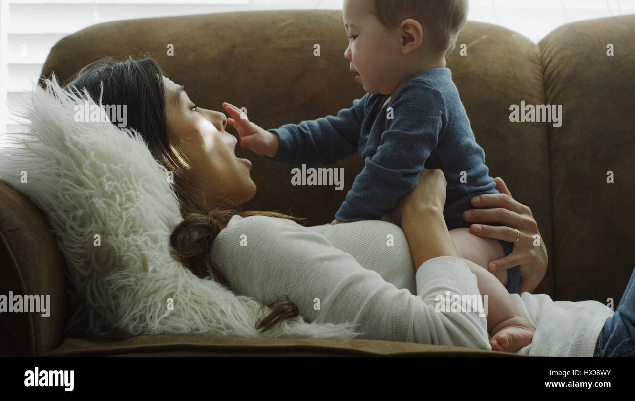 Profil von lachenden spielerische Mutter Baby Sohn halten und spielen auf sofa Stockfoto