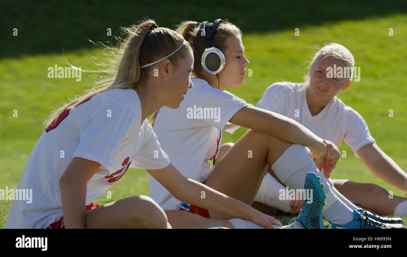 Höhenplan des Athleten hören Kopfhörer mit Teamkollege Fußball-Spieler sitzen auf Feld Stockfoto