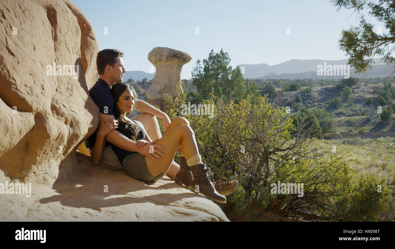Freund und Freundin sitzen auf felsigen Klippen, malerische Aussicht auf Felsen und Bäume in abgelegenen Wüstenlandschaft Stockfoto