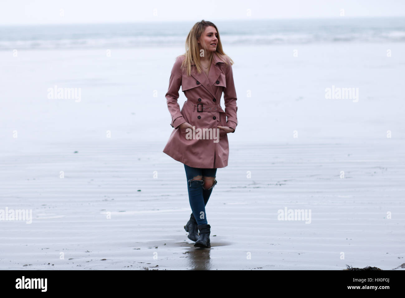 Junge blonde Frau trägt rosa Mantel auf Black Rock Sands Beach Stockfoto