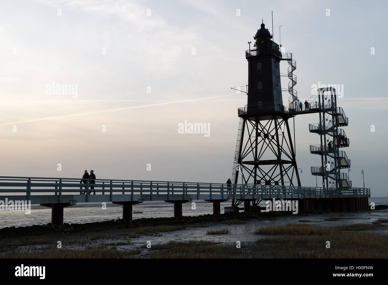 Dorum-Neufeld, Deutschland-11. März 2017: Besucher zu Fuß entlang der Pier der Leuchtturm Obereversand in malerischen Sonnenuntergang in der Nordsee Stockfoto