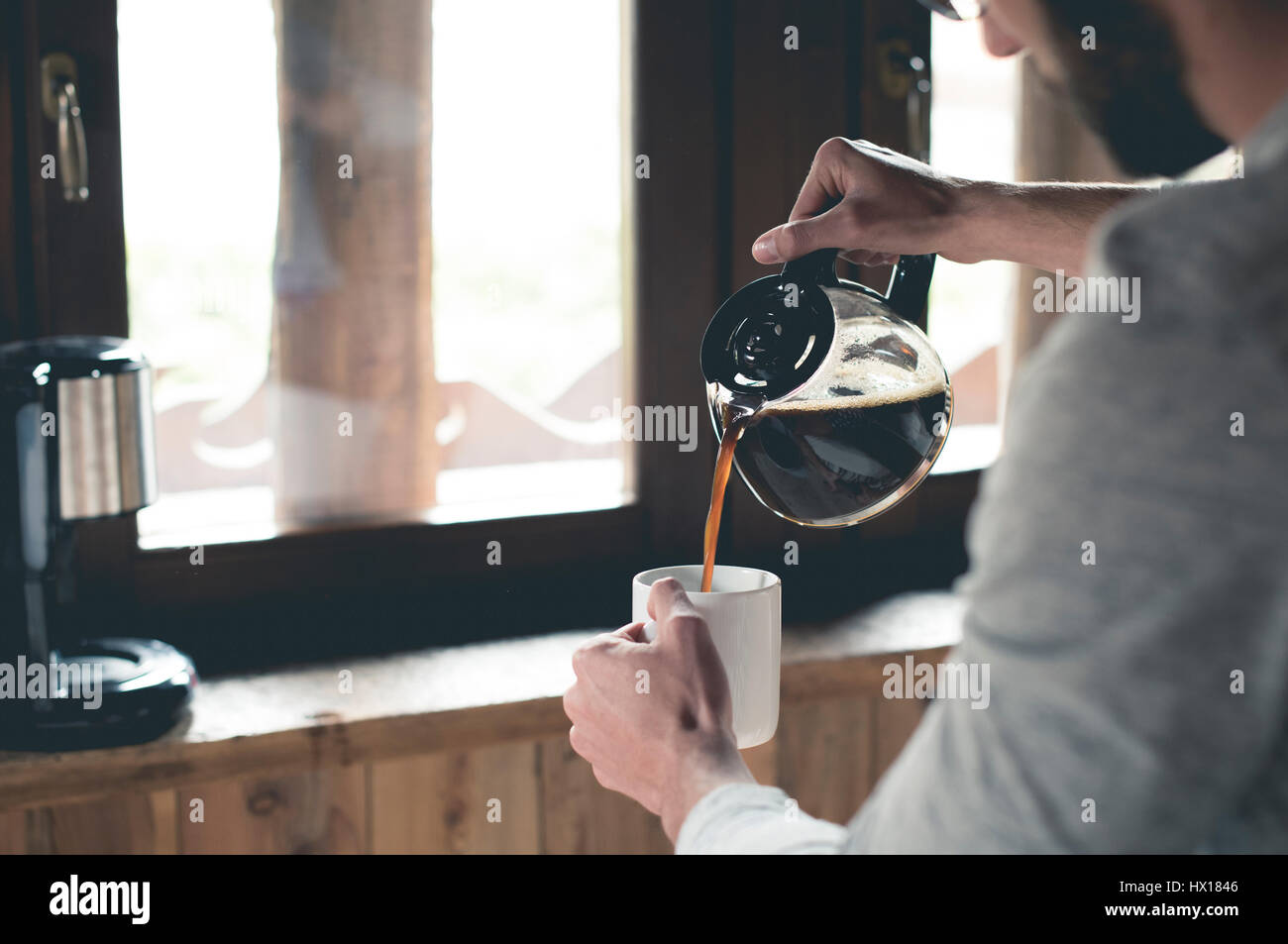 Junger Mann gießt Kaffee in der Tasse zu Hause Stockfoto