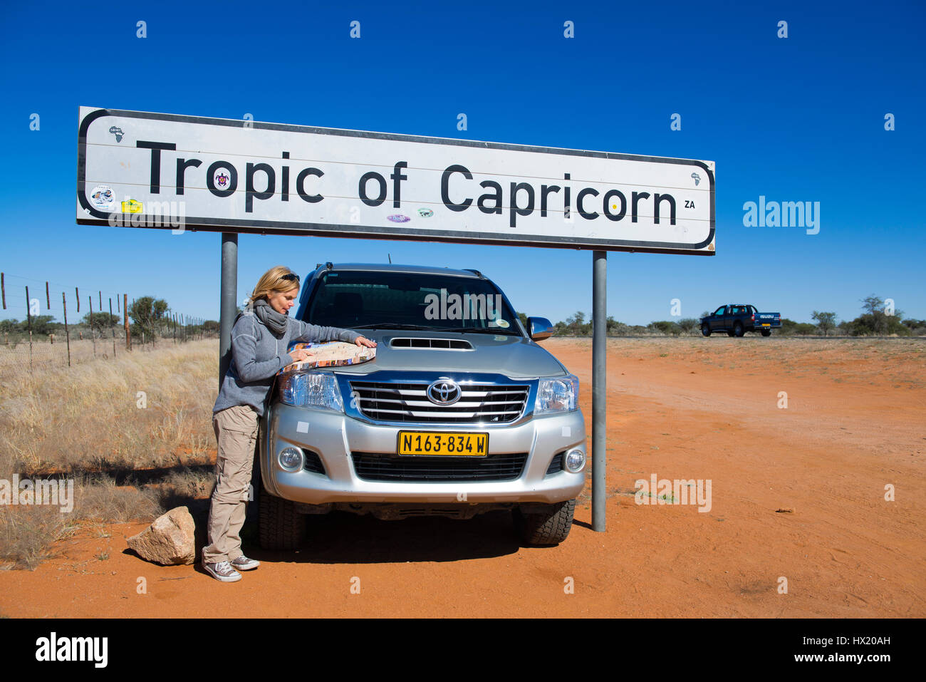 Frau mit Geländewagen steht ein Schild "Tropic of Caprocorn", in der Nähe von Rehoboth, Namibia Stockfoto