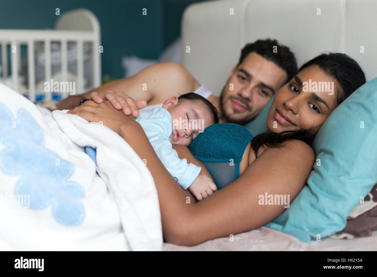 Junges Paar mit einem kuscheln im Bett mit ihrem sleepy Baby Sohn. Sie sind auf der Suche sowohl in die Kamera Lächeln. Stockfoto