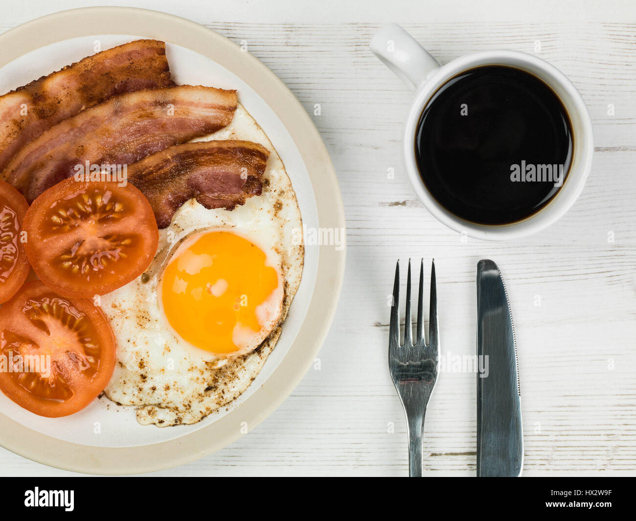 Authentische Flach bunte Englisches Frühstück, gebratenen Speck, Ei, Sunny Side Up, und gegrillten Tomaten mit einer Tasse starken Kaffee zurück Stockfoto