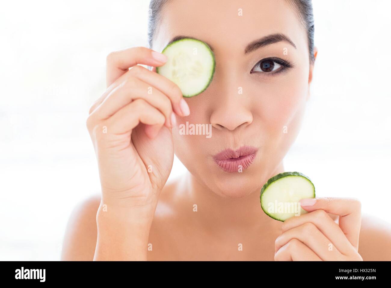 -MODELL VERÖFFENTLICHT. Junge asiatische Frau mit Gurke vor Auge, Porträt. Stockfoto