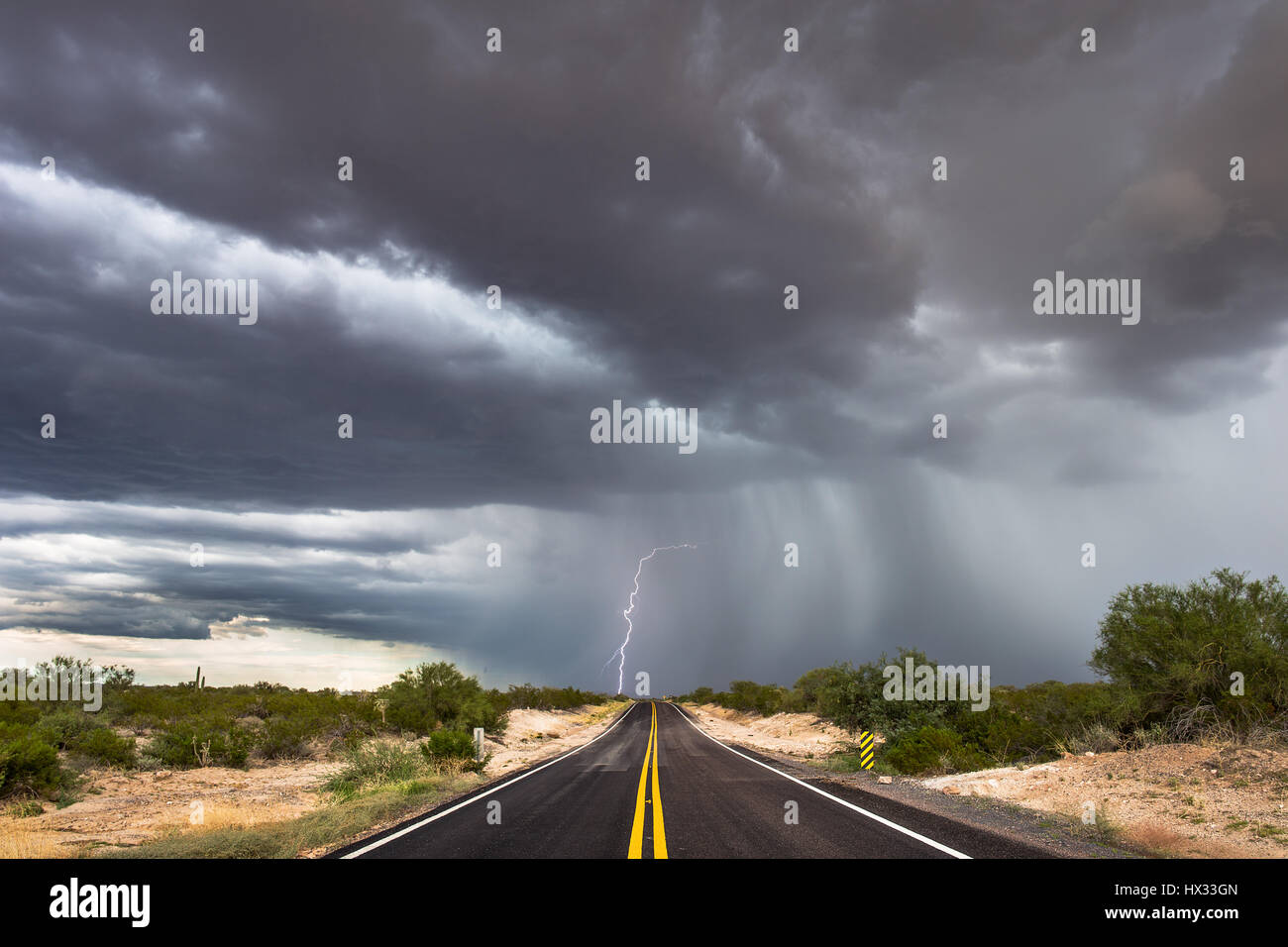 Dramatische Sturmwolken mit Blitzschlag am Ende einer leeren Straße in der Wüste von Arizona Stockfoto