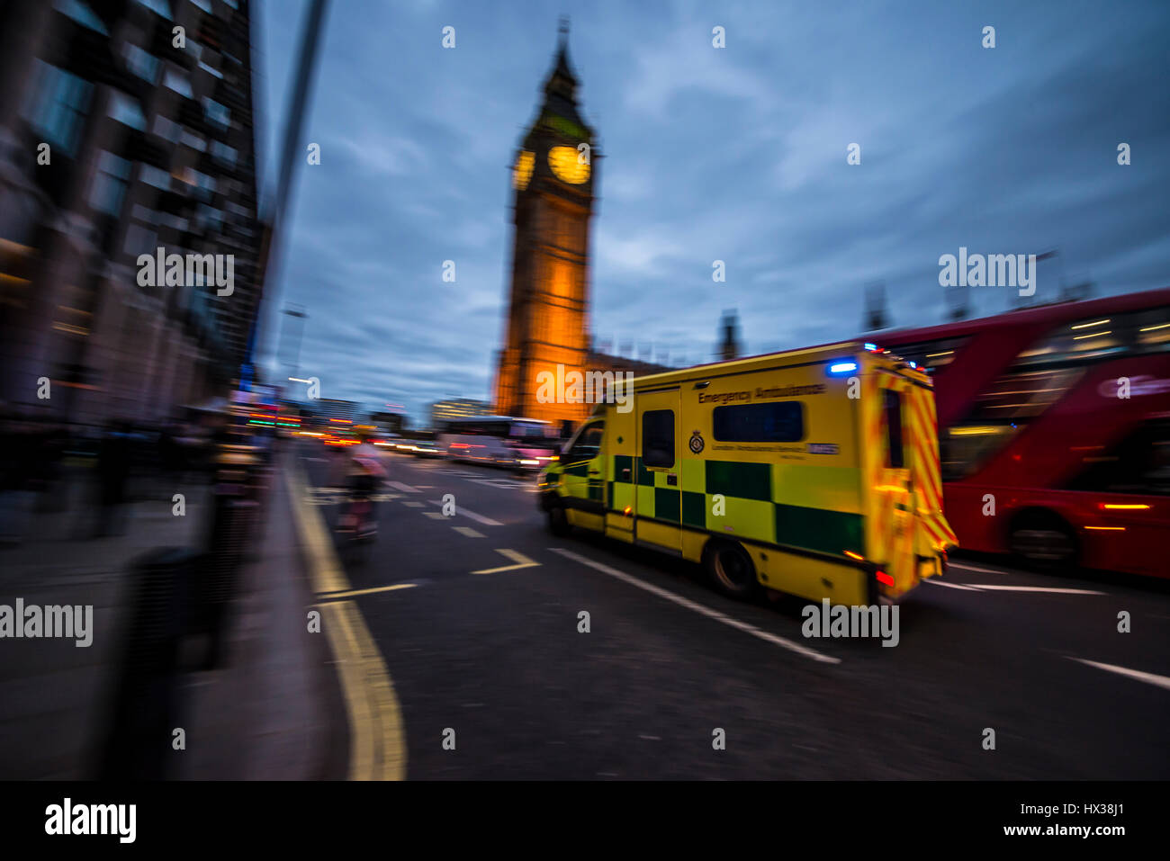 Ein Krankenwagen mit Geschwindigkeit in der Abenddämmerung mit blau Blaulicht vorbei an den Houses of Parliament in London vorbei an big Ben und einem roten Bus Reisen Stockfoto