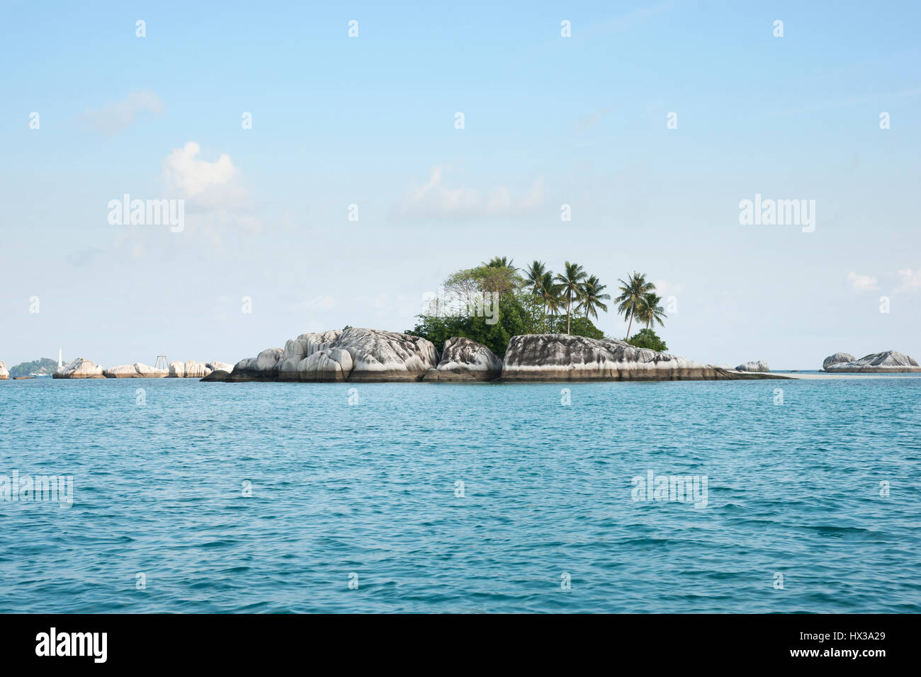 Natürliche Felsen im Meer mit grünen Palmen und Vegetation auf der Insel belitung am Nachmittag und einem weißen Leuchtturm im Hintergrund Stockfoto