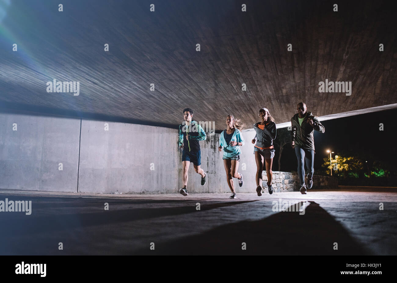 Gruppe junger Männer und Frauen zusammen in der Nacht laufen. Gesunde junge Menschen unter einer Brücke in der Stadt zusammen zu trainieren. Stockfoto