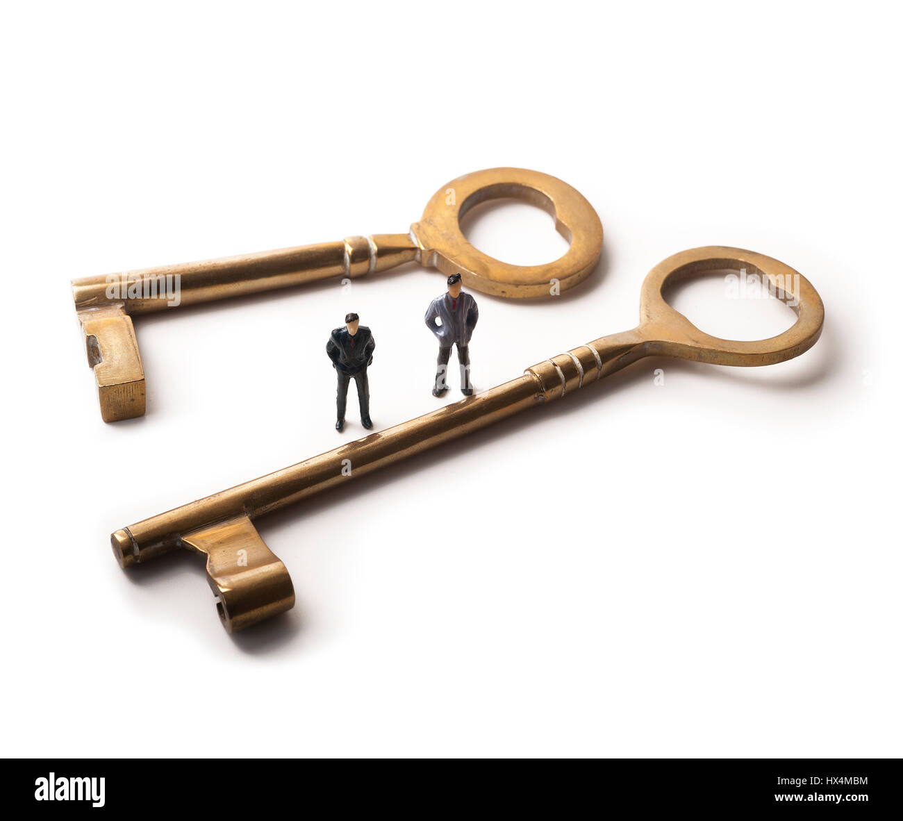 Zwei Miniaturfiguren stehen zwischen Messing Schlüssel unterschiedlicher Größe auf weißem Hintergrund Stockfoto