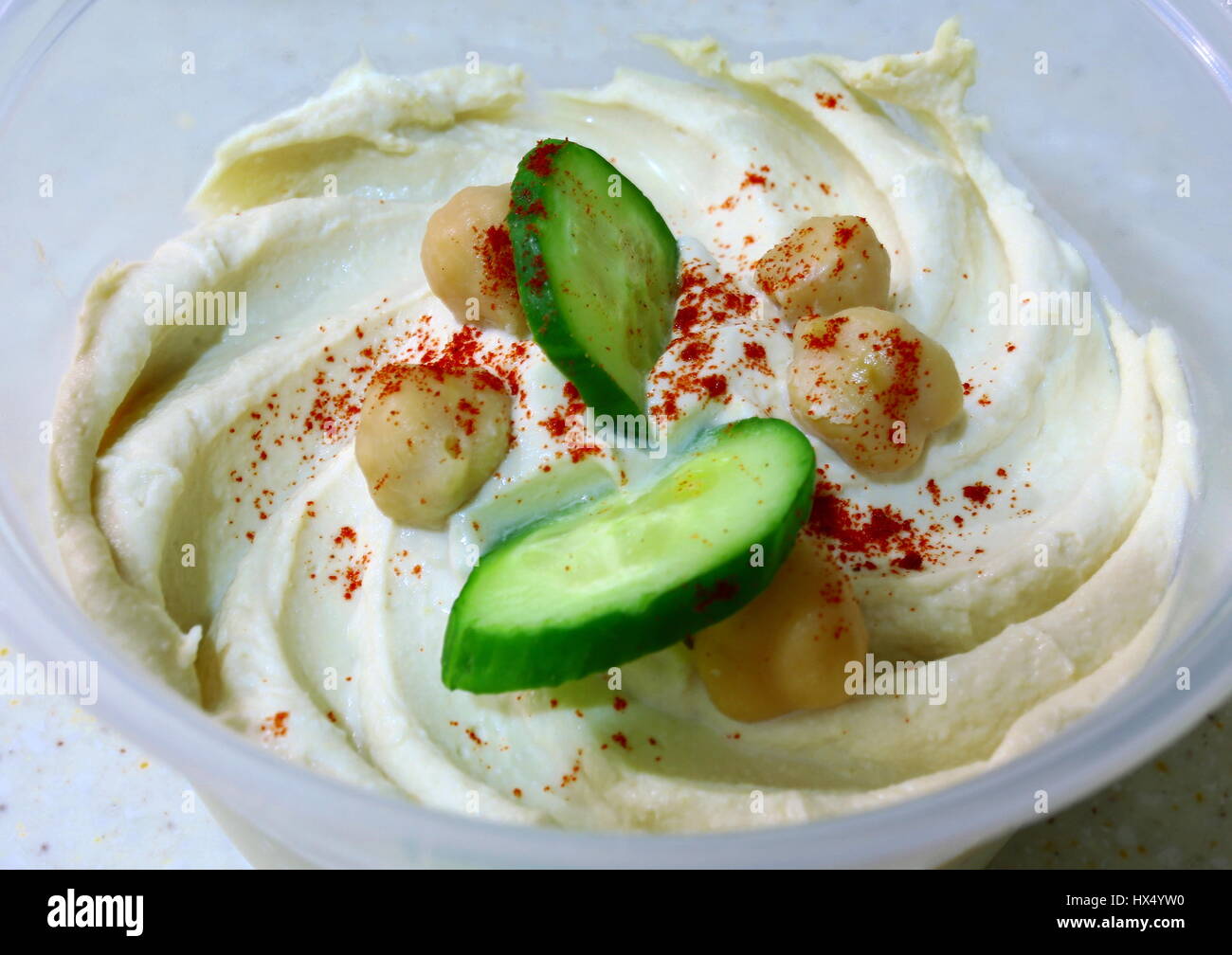 Ein Topf mit arabischen Hummus Kichererbsen, Tahin und Zitronensaft Dip garniert mit Gurkenscheiben, gekochte Kichererbsen und eine Prise paprika Stockfoto