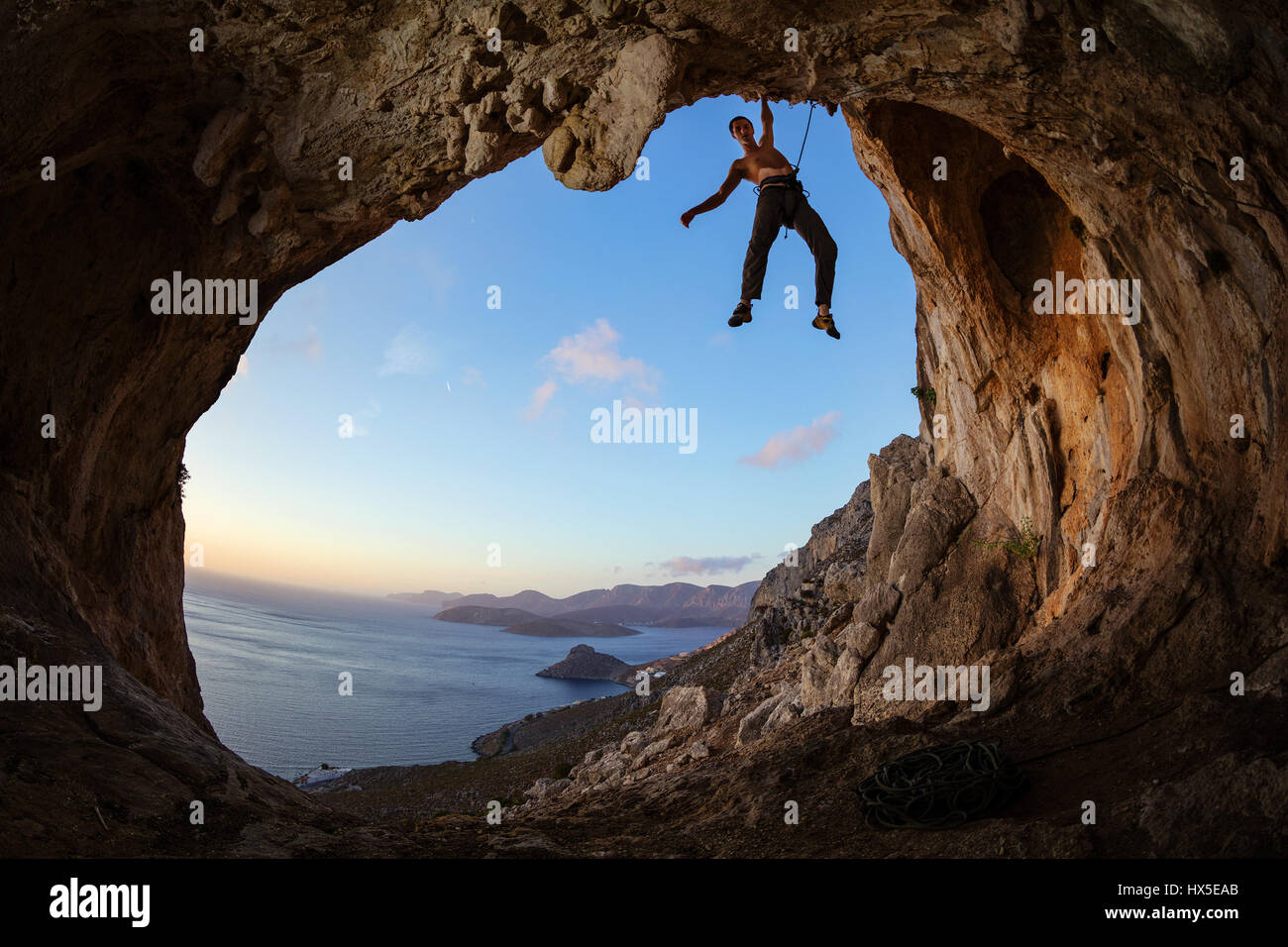 Kletterer greifen Haltegriff an Decke in Höhle gegen Blick auf Küste bei Sonnenuntergang Stockfoto