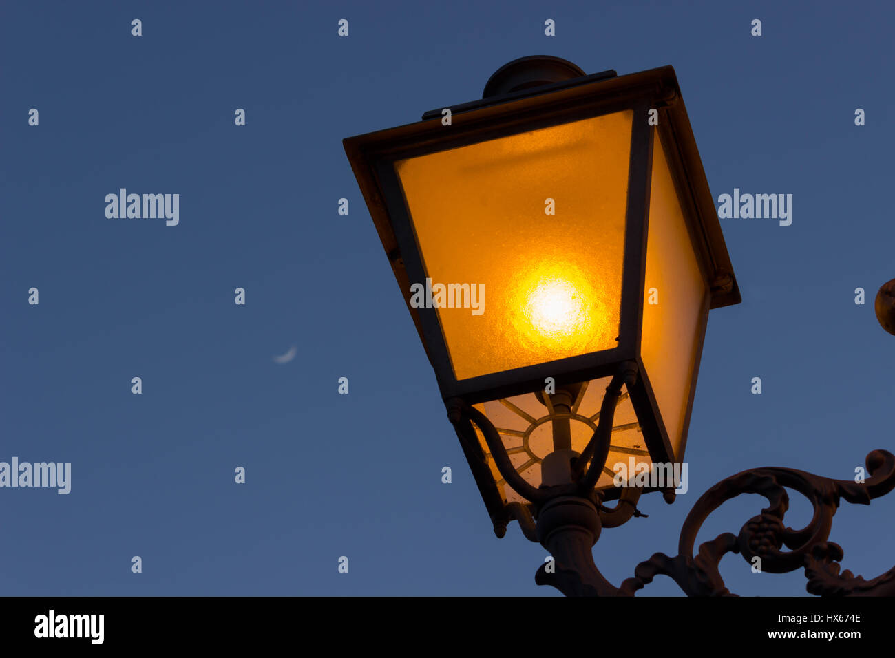 Eine Lampe am Abend mit einem Viertel Mond im Hintergrund Stockfoto