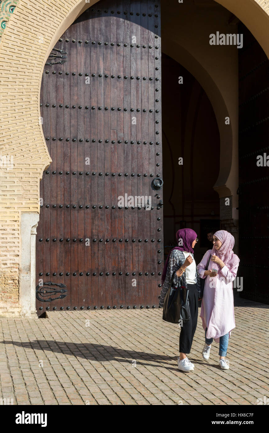 Meknès, Marokko.  Zwei junge Frauen in konservativen moderne Kleidung verlassen der Bab Mansour, ein Betrieb ein Handy. Stockfoto