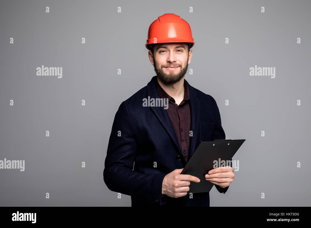 Mann in einem schwarzen Anzug und Bau Helm Blick zur Seite und halten schwarz auf grau Stockfoto
