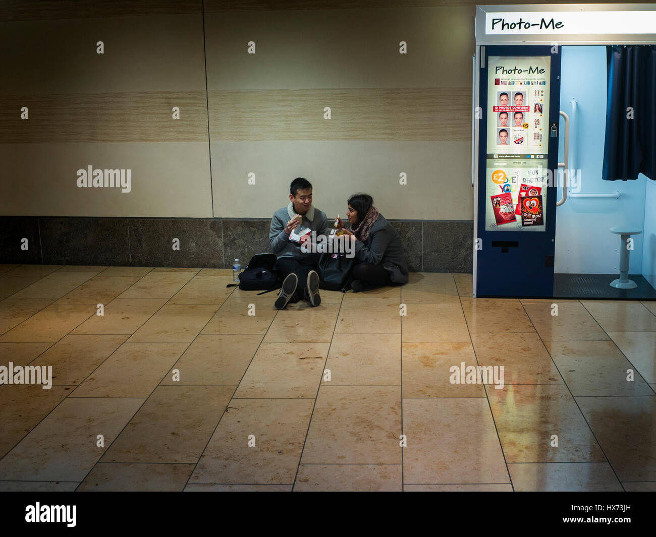 zwei Personen Essen am Boden neben einem Foto-mich schnellen Fotoautomaten in einem Einkaufszentrum in Cambridge Stockfoto