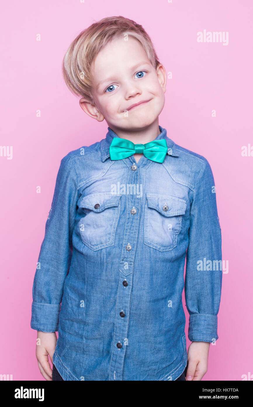 Junge hübsche Kind mit blauem Hemd und Krawatte Schmetterling lächelnd. Studio-Porträt über rosa Hintergrund Stockfoto