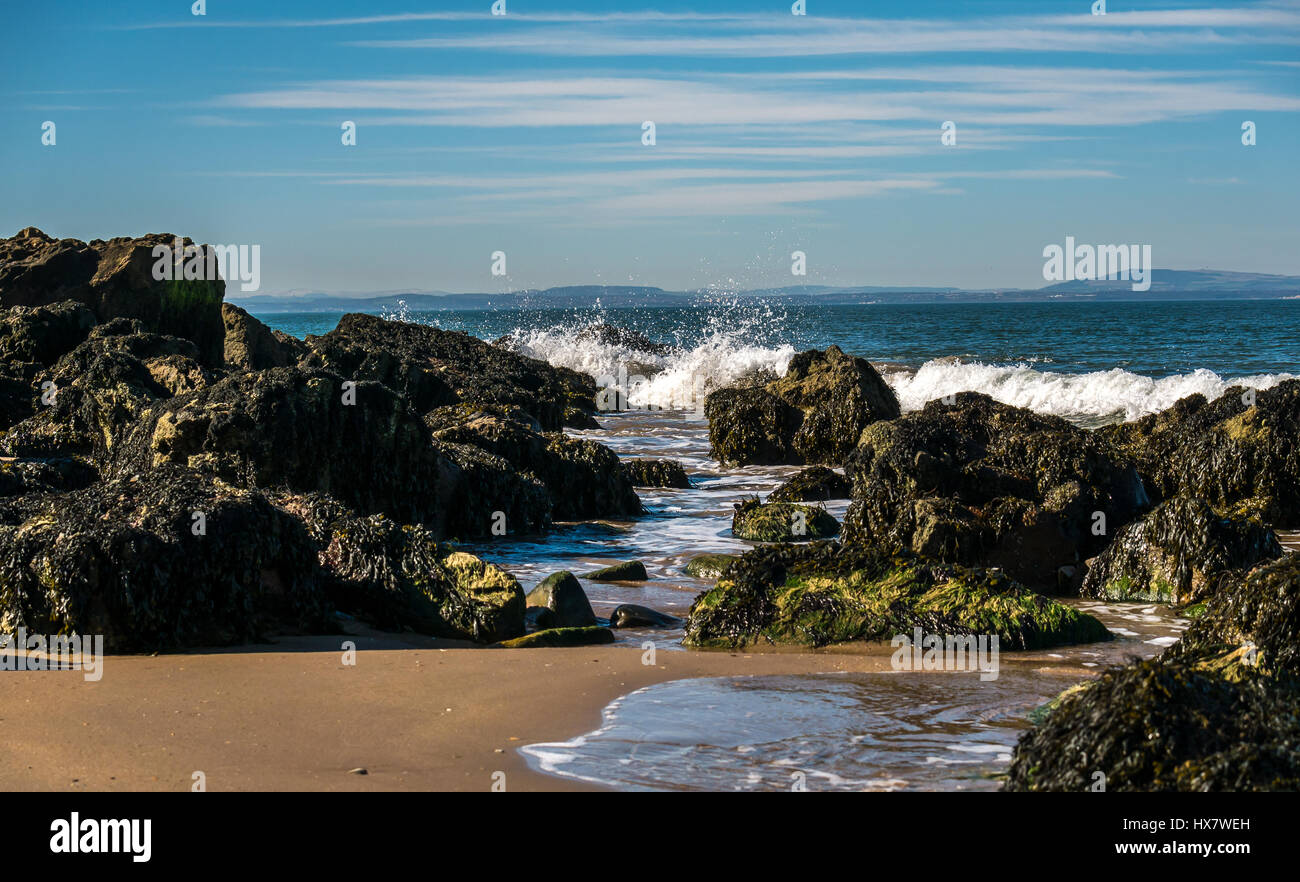 Wellen brechen an felsigen Küsten und am Strand an sonnigen Tagen, East Lothian, Schottland, Großbritannien Stockfoto