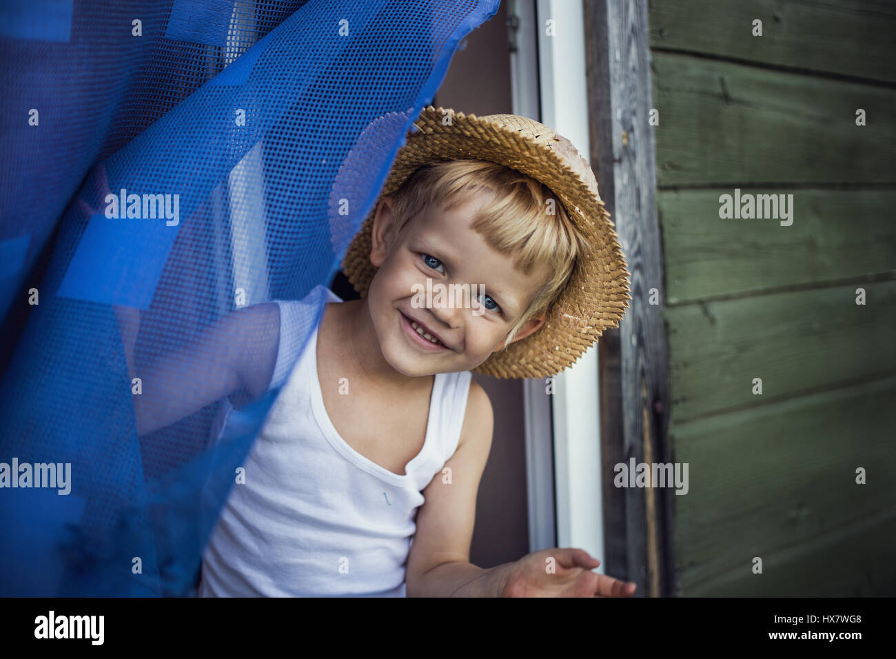 Outdoor-Porträt: fröhliches Kind mit Strohhut aus dem Fenster gelehnt Stockfoto