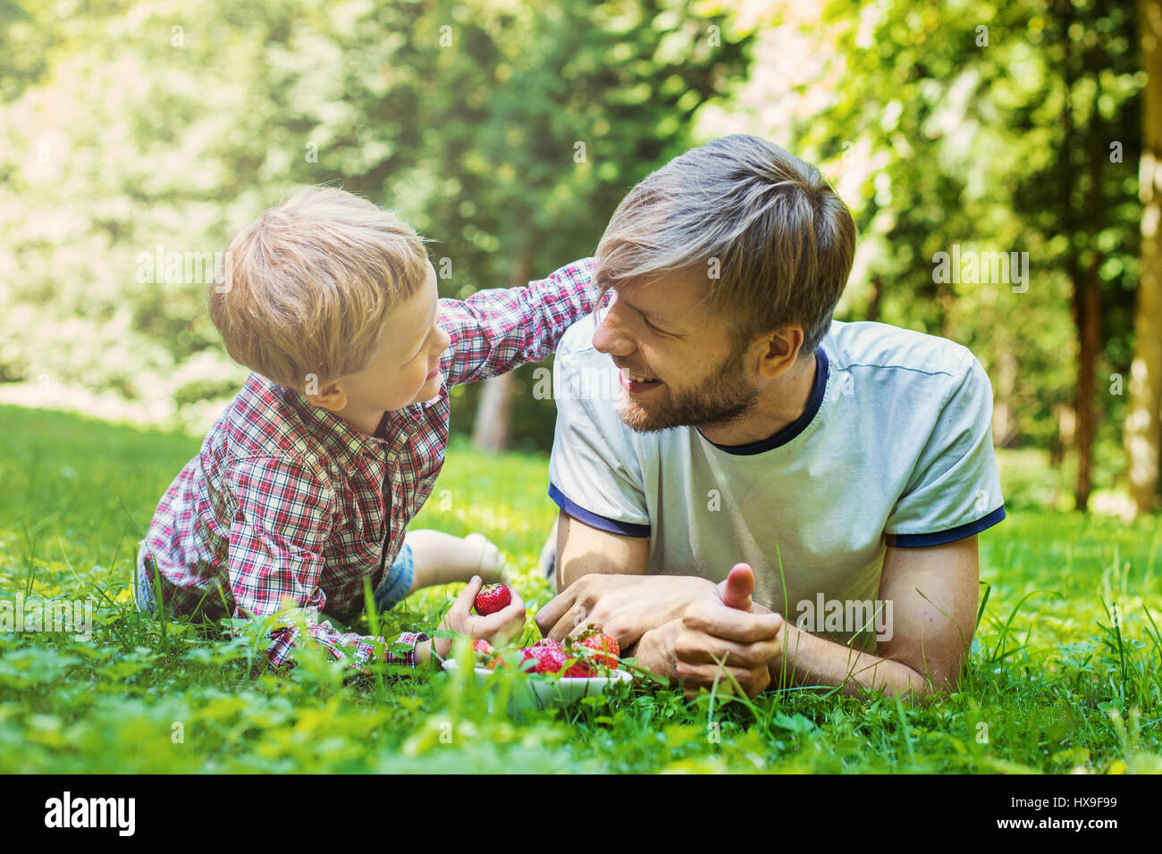 Junger Vater und sein Sohn Essen Erdbeeren im Park. Picknick. Outdoor portrait Stockfoto
