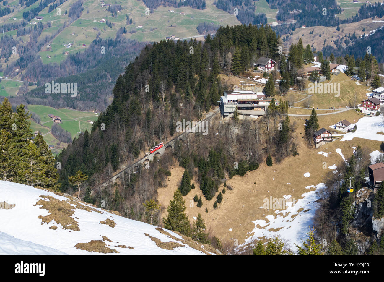 Rote Standseilbahn und gelbe Seilbahn Ankunft in ihren jeweiligen Bergstationen in Stoos, einem Bergdorf in der Zentralschweiz. Stockfoto