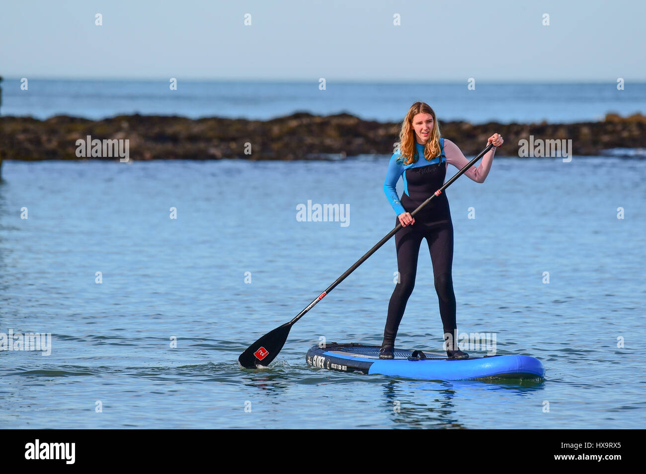Aberystwyth, Wales UK, Muttertag, Sonntag, 26. März 2017 UK Wetter: eine junge Frau in einen Neoprenanzug Paddel auf ihre SUB (Stand-up Board) auf das flache Meer. Es ist ein anderer Tag von strahlendem Sonnenschein und blauem Himmel in Aberystwyth an der Westküste von Wales klar. Bildnachweis: Keith Morris/Alamy Live-Nachrichten Stockfoto