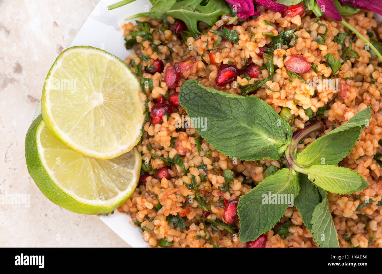 Vegetarische Kost - orientalische Speisen, bestehend aus Bulgur-Weizen-Salat, Raketen, Sauerkraut Limetten und Minze - Konzept - gesunde Ernährung Stockfoto