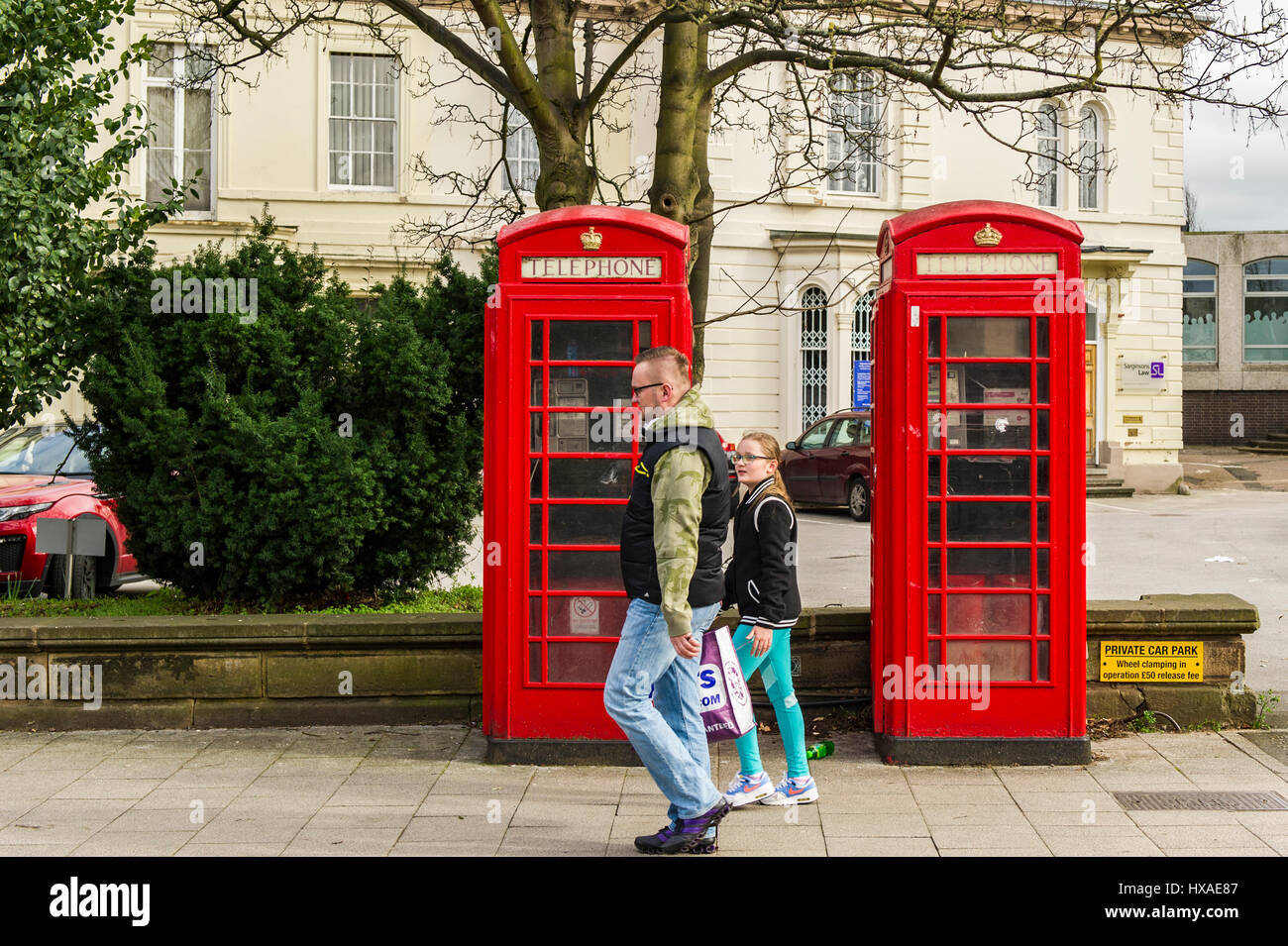 Mann und junge Mädchen zu Fuß vorbei an zwei roten alten altmodischen Telefonzellen in Coventry, Vereinigtes Königreich. Stockfoto