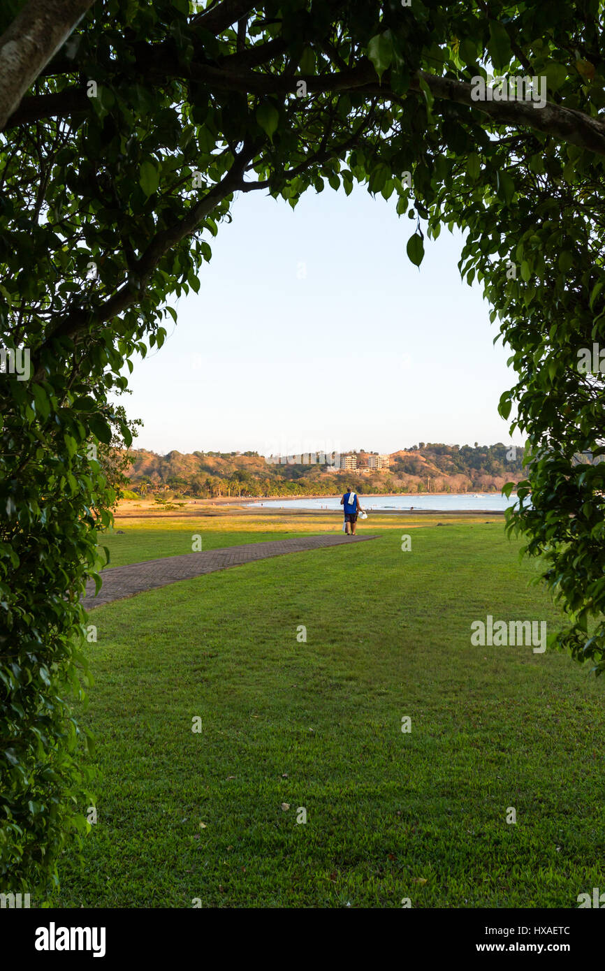 Paare, die an Stationen am Strand am Nachmittag durch einen Ausschnitt auf einer großen Hecke gesehen Stockfoto