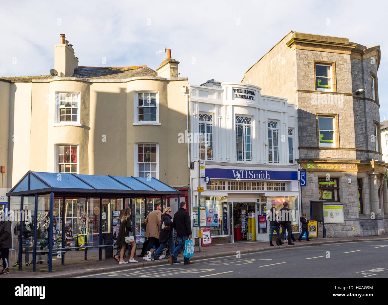 Eine Schlange von Menschen an einer Bushaltestelle direkt vor einem WH Smith-Shop in Teignmouth, Devon, UK. Stockfoto