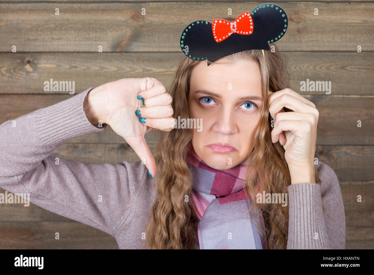 Junge Frau mit lustigen Frisur auf einem Stick zeigt Daumen runter Zeichen, hölzernen Hintergrund. Spaß Foto Requisiten und Zubehör für Shootings Stockfoto