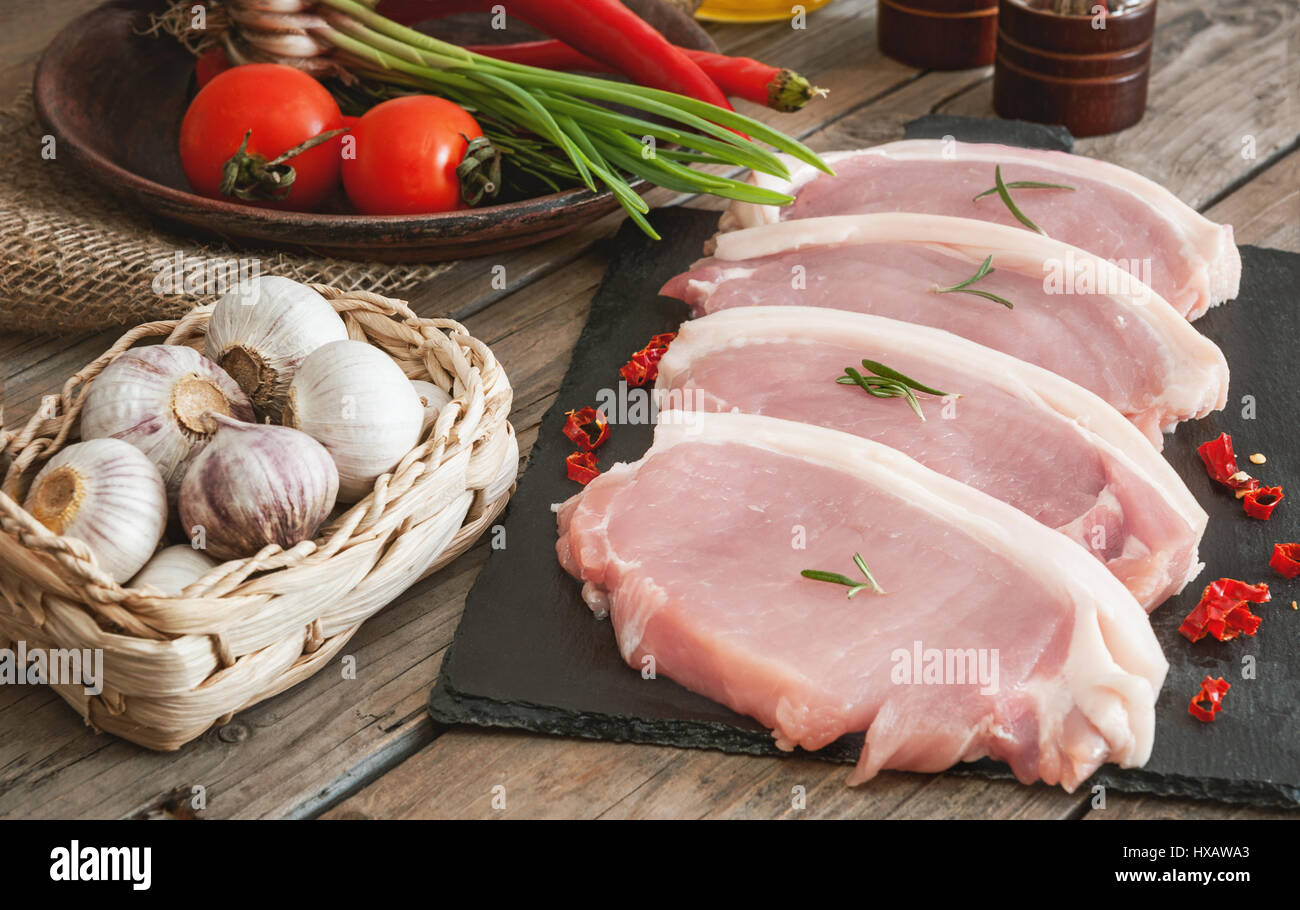 Stücke vom Schwein zum Grillen auf Schiefer Board mit Rosmarin, Knoblauch in einem Weidenkorb, Tomaten im rustikalen Stil Stockfoto