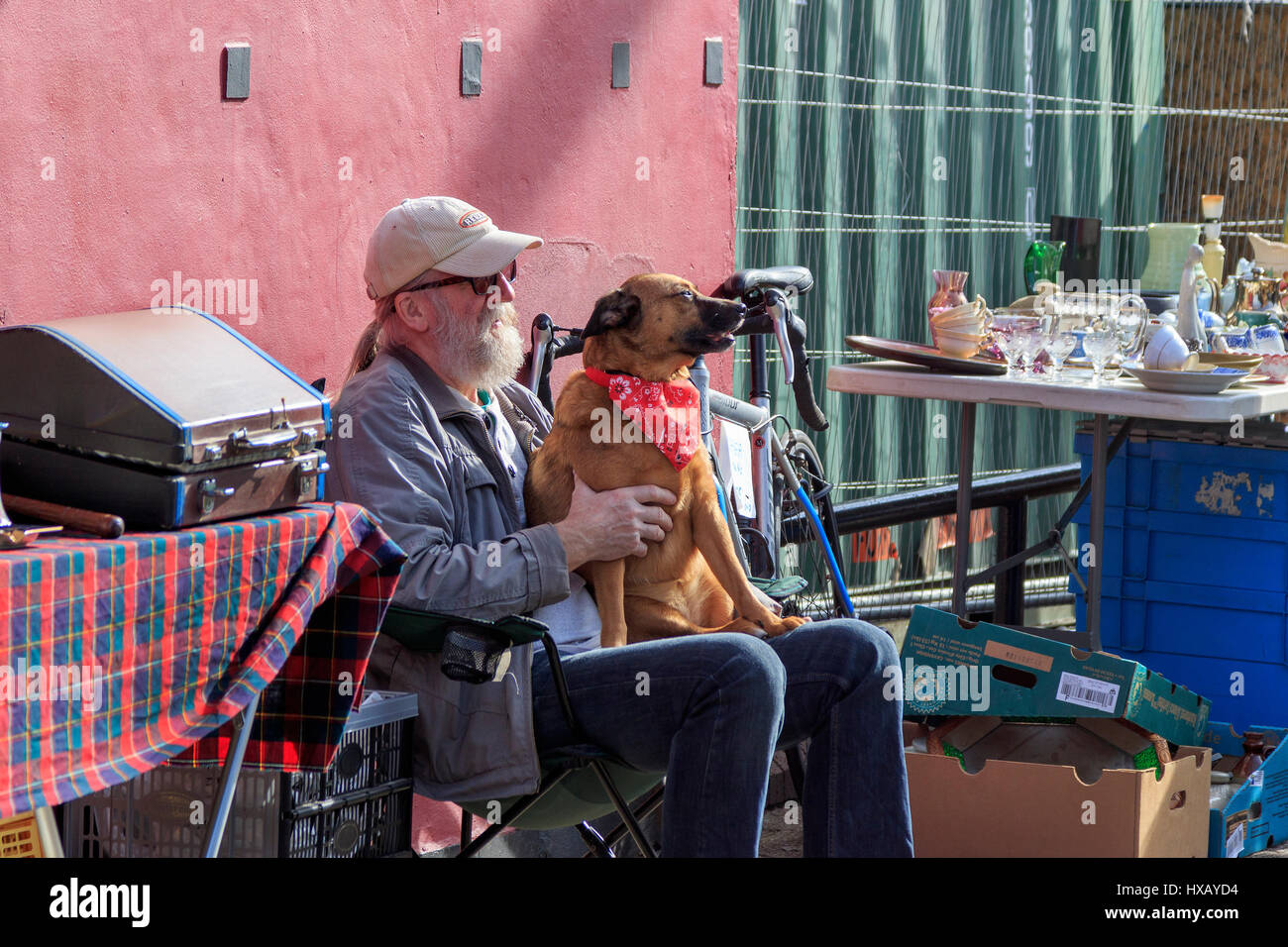 Standbesitzer in Glasgow's berühmten Barras open air und Street Market, in der Sonne zu sitzen Streichelzoo mit seinem Hund. Glasgow. Schottland.DE Stockfoto