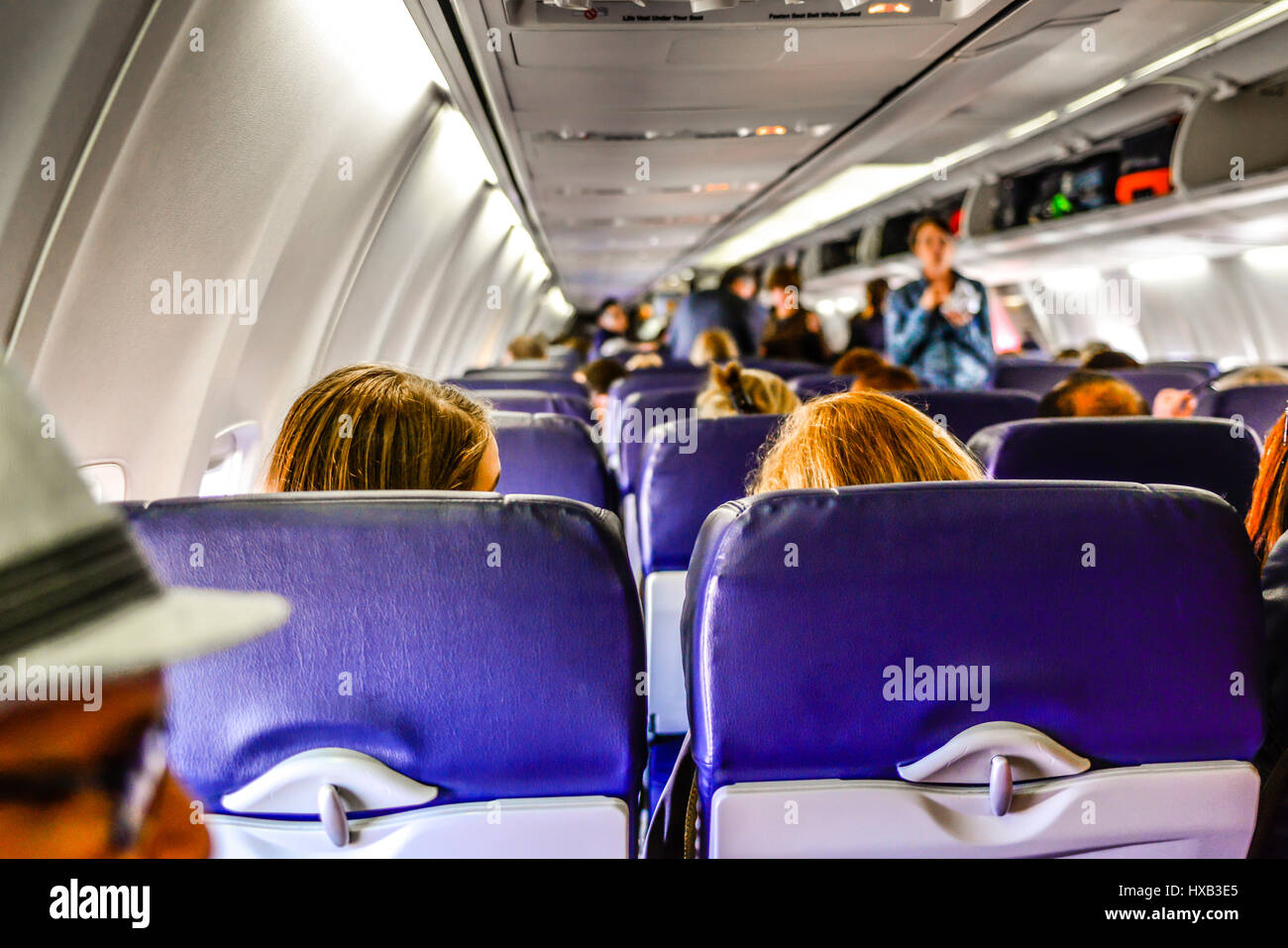 Ein Blick von der Rückseite eines kommerziellen Flugzeug der Kabine mit Menschen einsteigen, sitzen & Gepäckfächer verwenden, während Flugbegleiter schauen auf Stockfoto