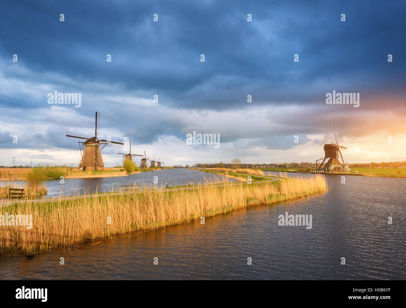 Erstaunliche Windmühlen. Rustikale Landschaft mit traditionellen holländischen Windmühlen in der Nähe von Wasserkanälen und blauen Wolkenhimmel und gelben Sonnenlicht. Farbenprächtigen Sonnenuntergang in Stockfoto