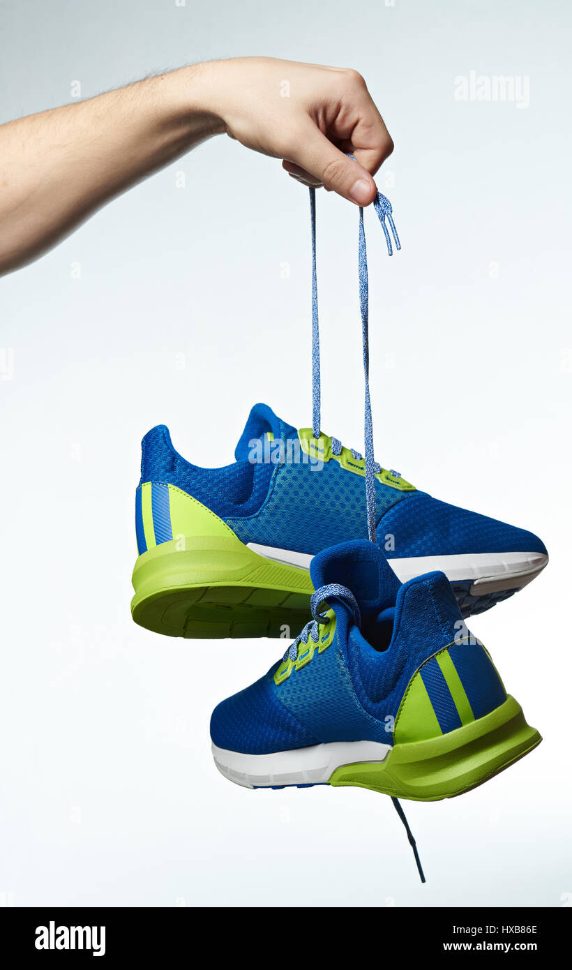 Hand mit bunten Laufschuhe isoliert auf weißem Hintergrund. Sportschuhe hängen am Schnürsenkel Stockfoto