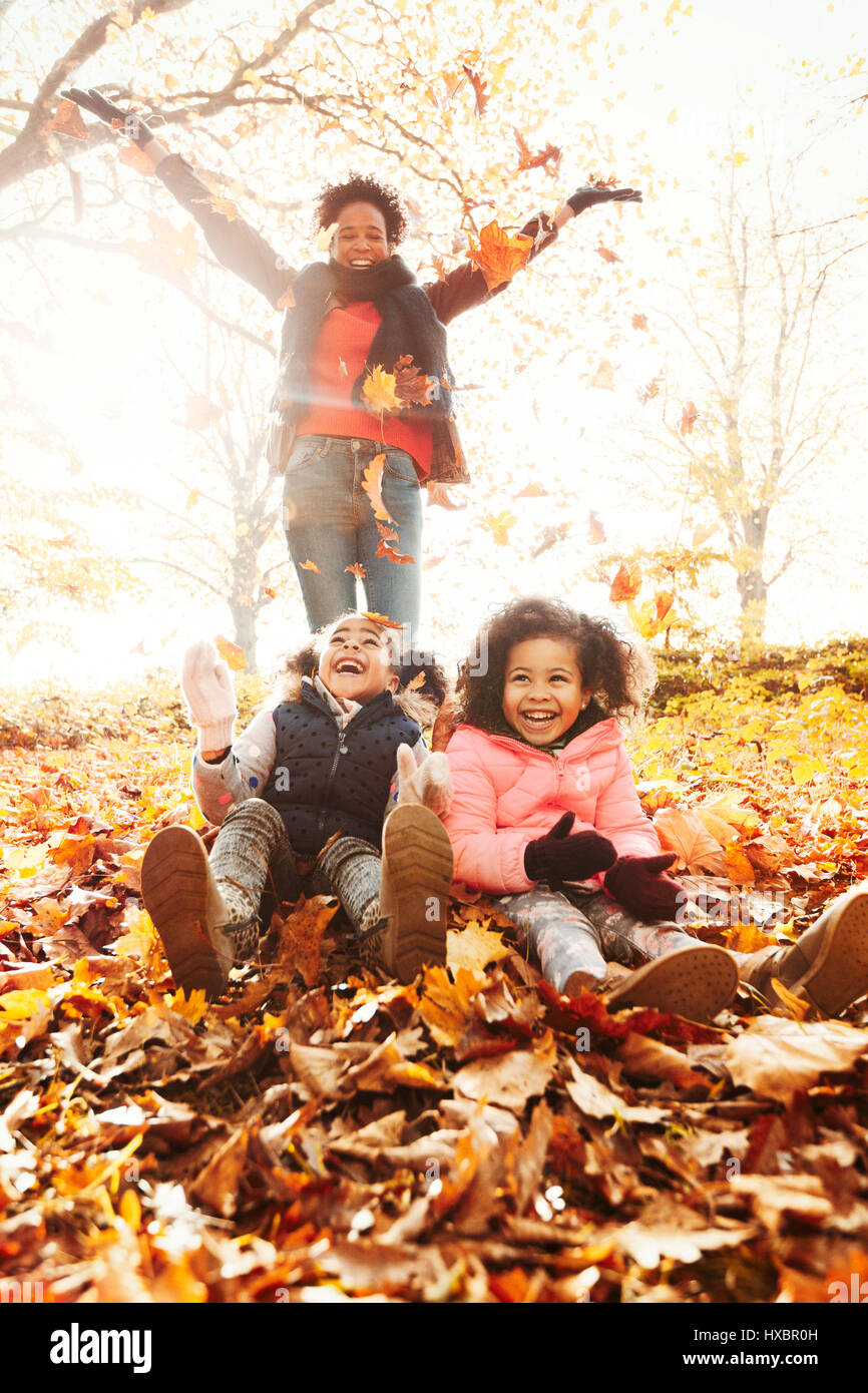 Spielerische Mutter und Töchter werfen Herbstlaub im sonnigen park Stockfoto