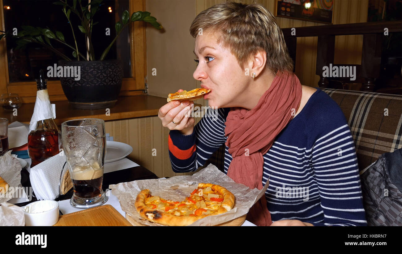 Hübsche blonde Frau Pizza isst und trinkt Bier Stockfoto