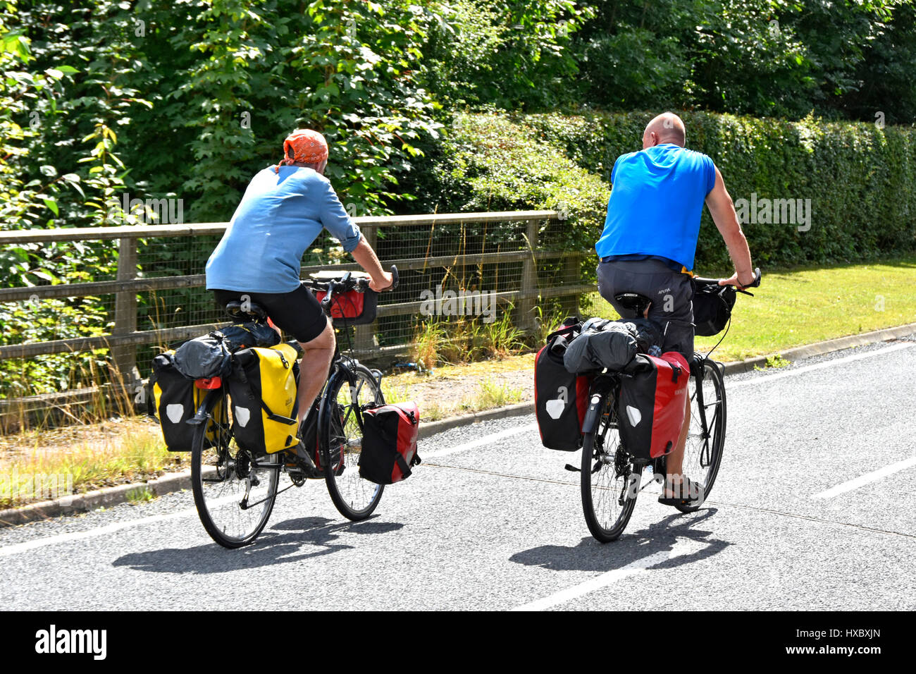 Paar Radfahren englische Straße auf Radweg für Fahrrad entlang ruhigen Landstraße in Essex England UK im Sommersonnenschein mit Fahrrad Packtaschen ausgestattet Stockfoto