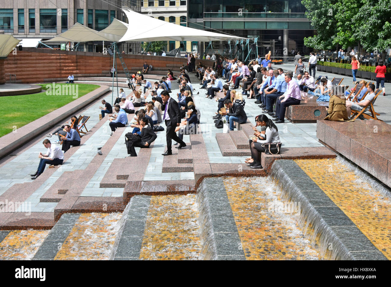 London Frauen Männer weibliche und männliche Büro Arbeiter Arbeiter uk Mittagspause Entspannung im Sonnenschein im Sommer Saison viele Snacks Essen neben Brunnen Wasserspiel Stockfoto